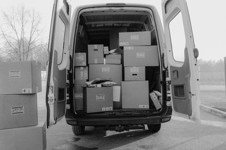 A black and white photograph shows a narrow, curved brick driveway in an urban residential area, with two white box trucks parked side by side along the curb. The trucks are positioned parallel to the