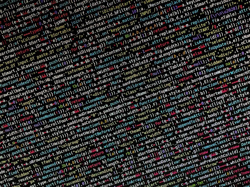 A photograph of a computer screen displaying colorful lines of source code with syntax highlighting, including various programming language elements such as functions, variables, and tags in multiple 